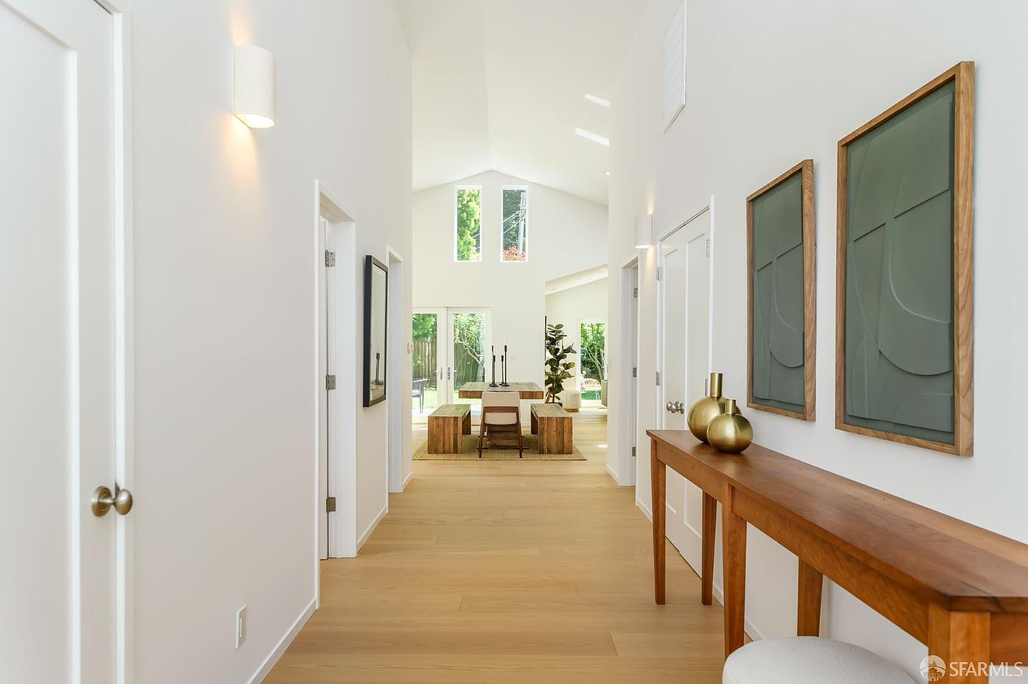 Long entry gallery with vaulted ceiling, sconce lighting, and view through to the dining and garden beyond