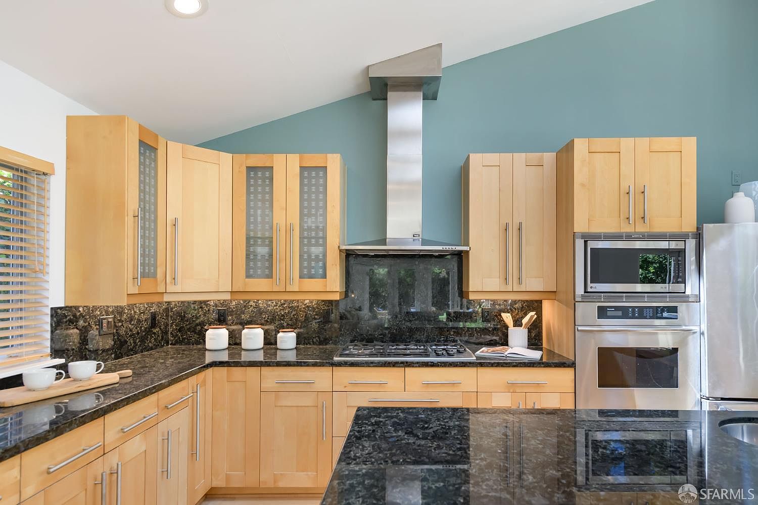 Kitchen with maple cabinetry, granite counters, stainless range hood, and a teal accent wall