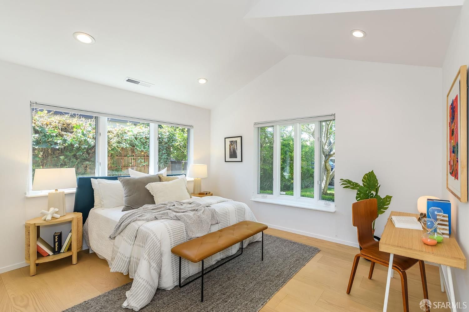 Primary bedroom with vaulted ceiling, deep blue upholstered headboard, garden views from three sides